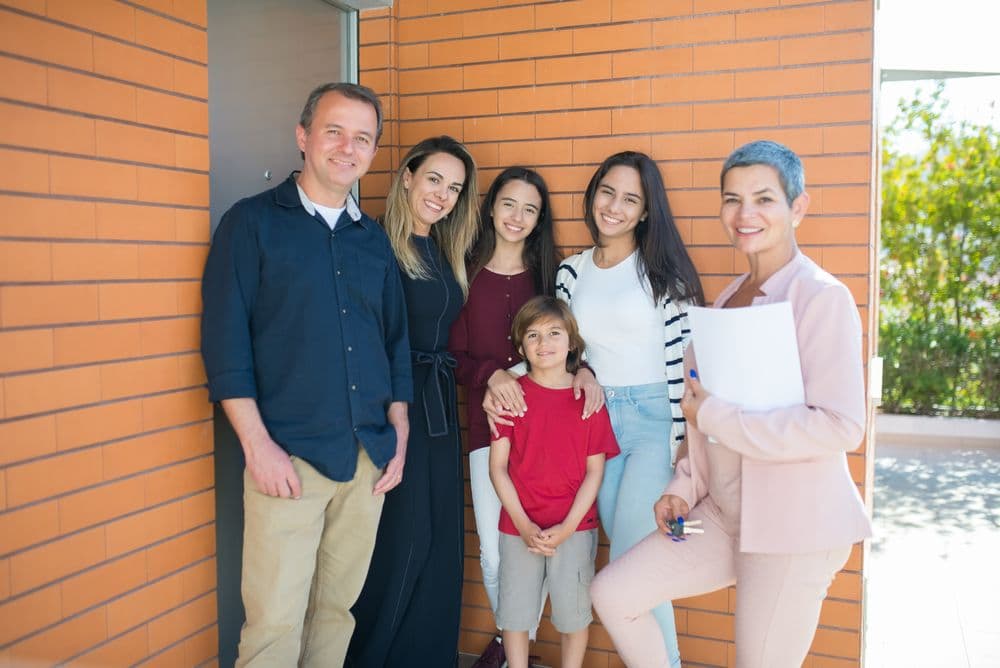 A family standing with their agent outside a new home, smiling together.