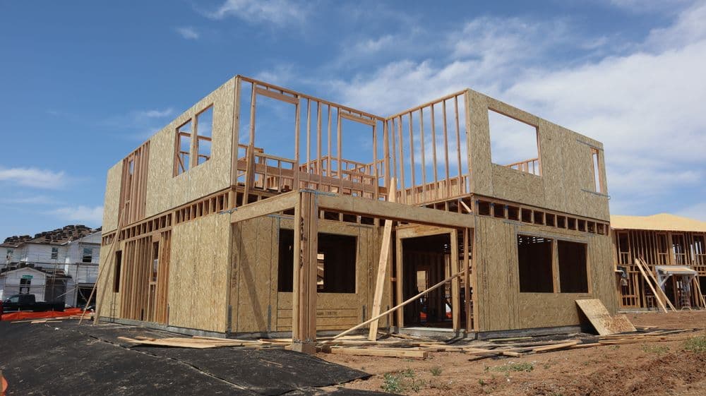 A new two-story home under timber-frame construction against a blue sky.