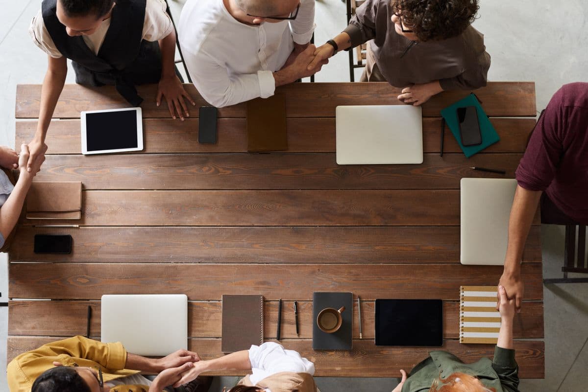 A diverse team collaborating around a table, shaking hands over laptops and notes.