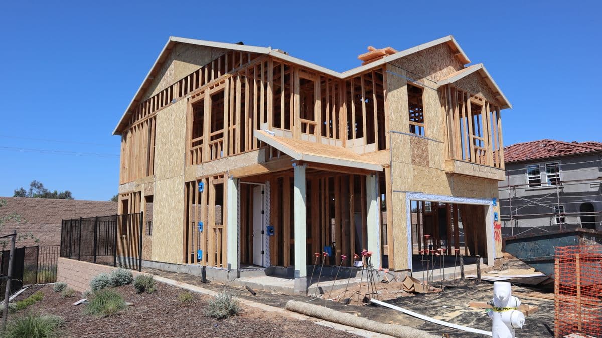 A new single-family home under construction, framed in timber against a clear California sky.